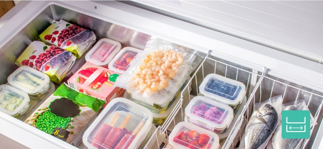 Wnętrze zamrażarki wypełnione różnorodnymi produktami spożywczymi, w tym mrożonymi owocami, warzywami, krewetkami i rybami. Na dole obrazu widoczna jest ikona z symbolem zamrażarki.