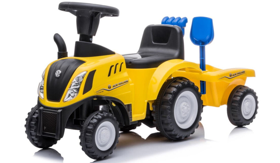 Żółty jeździk w kształcie traktora z przyczepą, posiada czarne siedzenie i kierownicę. Na boku widoczny napis \'New Holland\'.