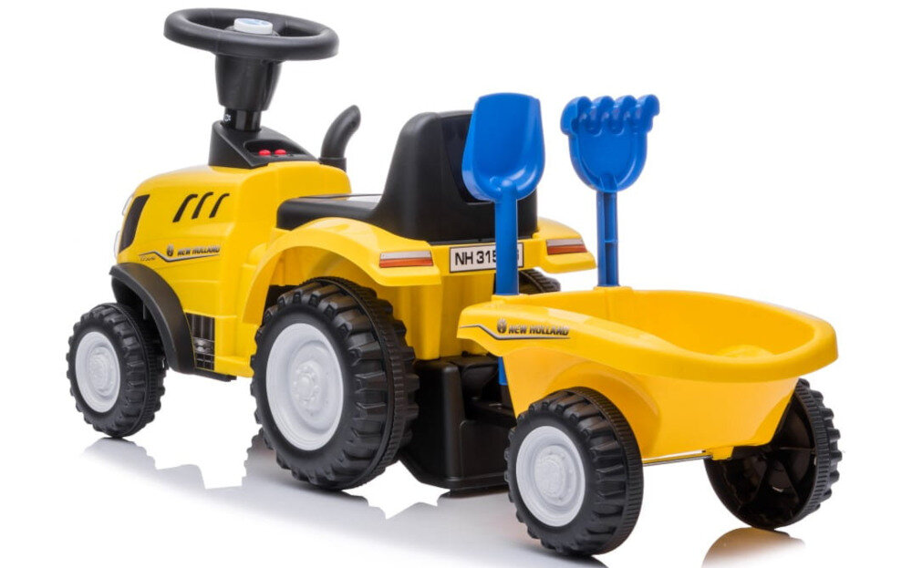 Żółty jeździk w kształcie traktora z przyczepą, wyposażony w kierownicę i dwa niebieskie narzędzia ogrodowe. Na boku widoczny jest napis \'New Holland\'.