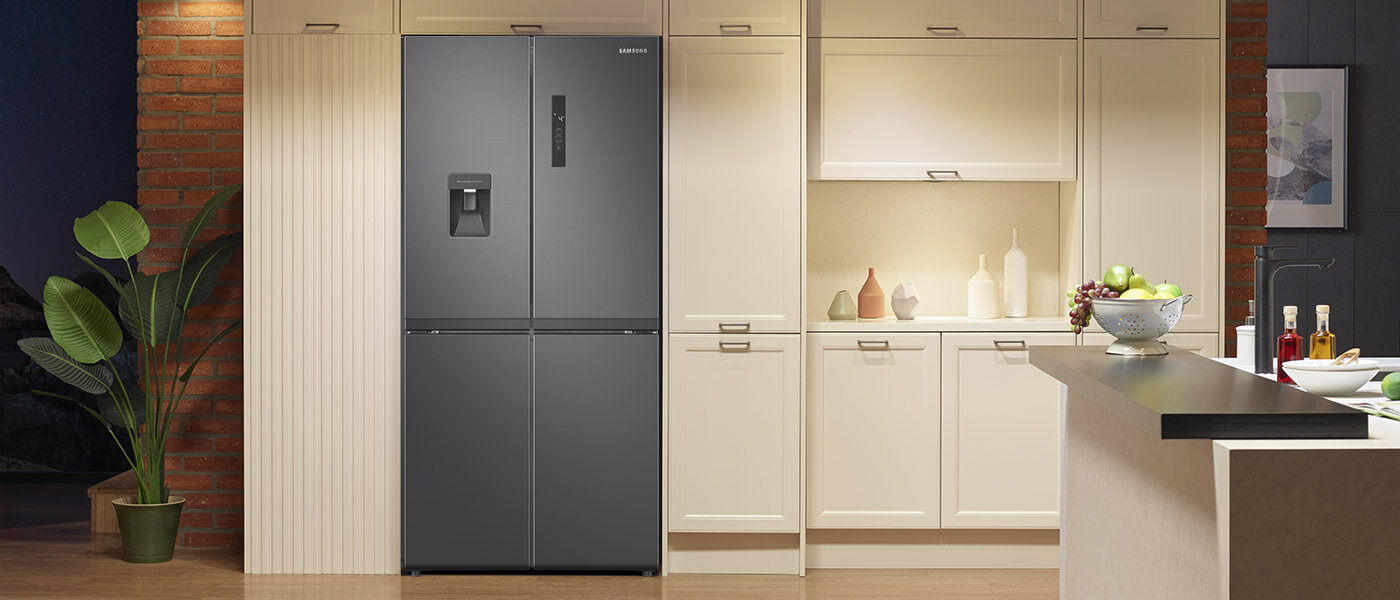 Lodówka Multidoor Samsung RF48A401EB4 wyróżnia się eleganckim designem i płaskimi drzwiami w kolorze srebrnym Grafitowa lodówka z dwoma drzwiami i wbudowanym dystrybutorem wody stoi w nowoczesnej kuchni. Obok znajdują się jasne szafki kuchenne i dekoracje, takie jak rośliny i miska z owocami.