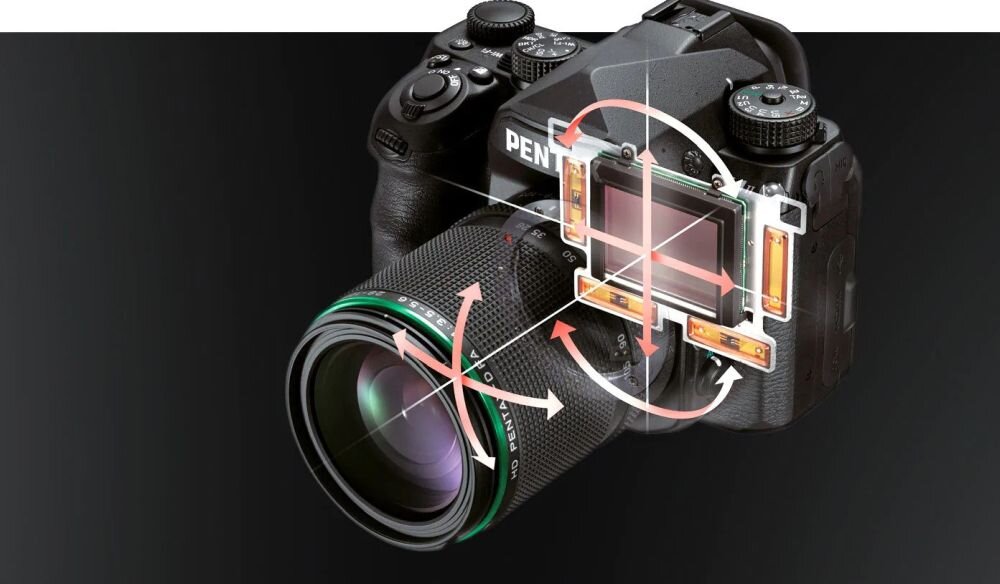 Na obrazie widoczna jest lustrzanka cyfrowa z logo PENTAX, z wizualizacją mechanizmu stabilizacji matrycy. Aparat ma duży obiektyw z zielonym pierścieniem.