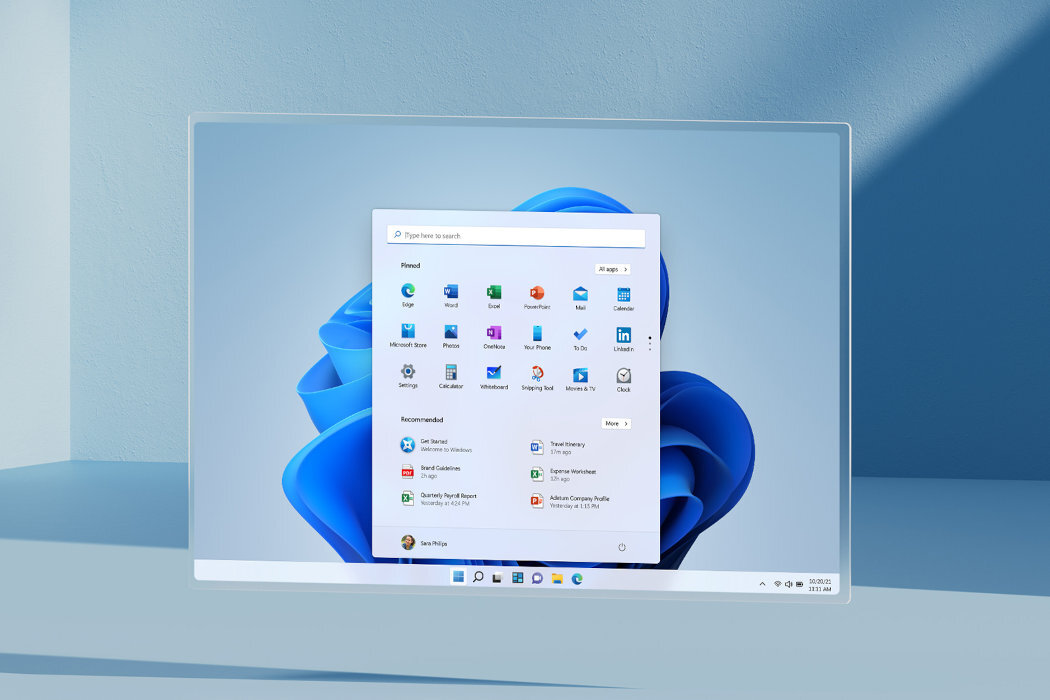 Obraz przedstawia ekran komputera z otwartym menu startowym systemu Windows 11, na którym widoczne są ikony aplikacji oraz pasek zadań u dołu. W tle znajduje się niebieska tapeta z abstrakcyjnym wzorem.