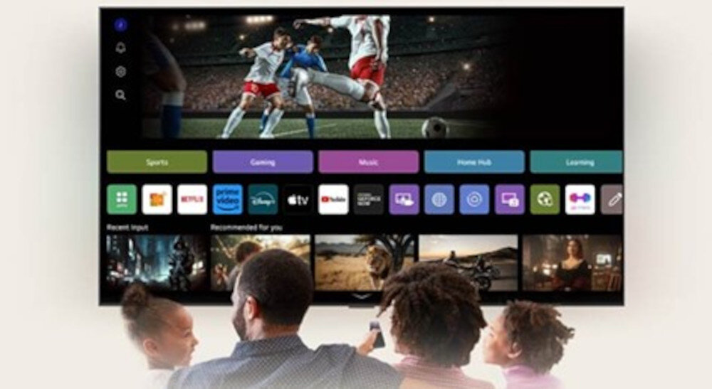 Na ekranie telewizora wyświetlany jest mecz piłki nożnej oraz interfejs z aplikacjami takimi jak Netflix, Prime Video i YouTube. Przed telewizorem siedzą cztery osoby, patrząc na ekran.