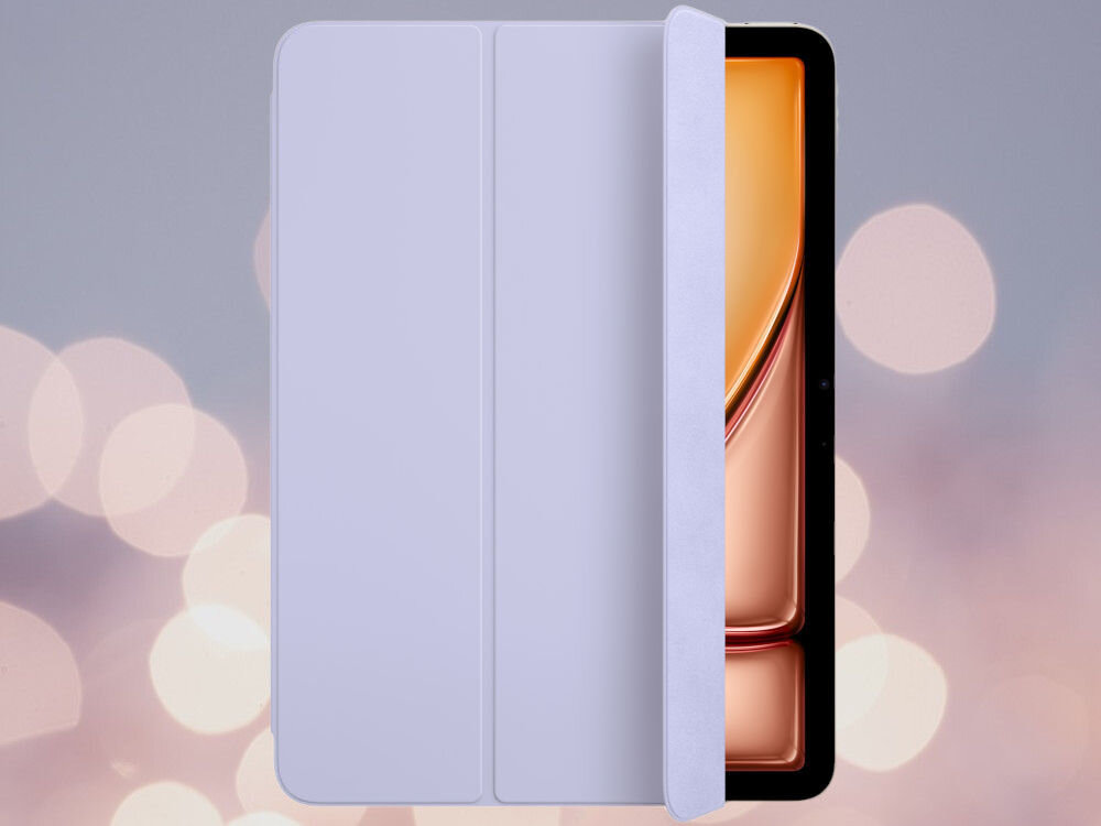 Etui na iPad w jasnym fiołkowym kolorze, częściowo zakrywające ekran urządzenia z widocznym pomarańczowym tłem. W tle rozmyte, jasne okręgi na szarym tle.