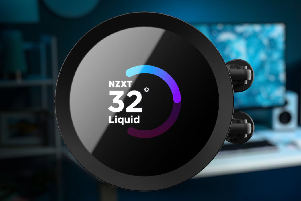Obraz przedstawia okrągły wyświetlacz z napisem \'NZXT 32° Liquid\' oraz kolorowym wskaźnikiem temperatury. W tle widoczne jest rozmyte wnętrze z biurkiem i monitorem.