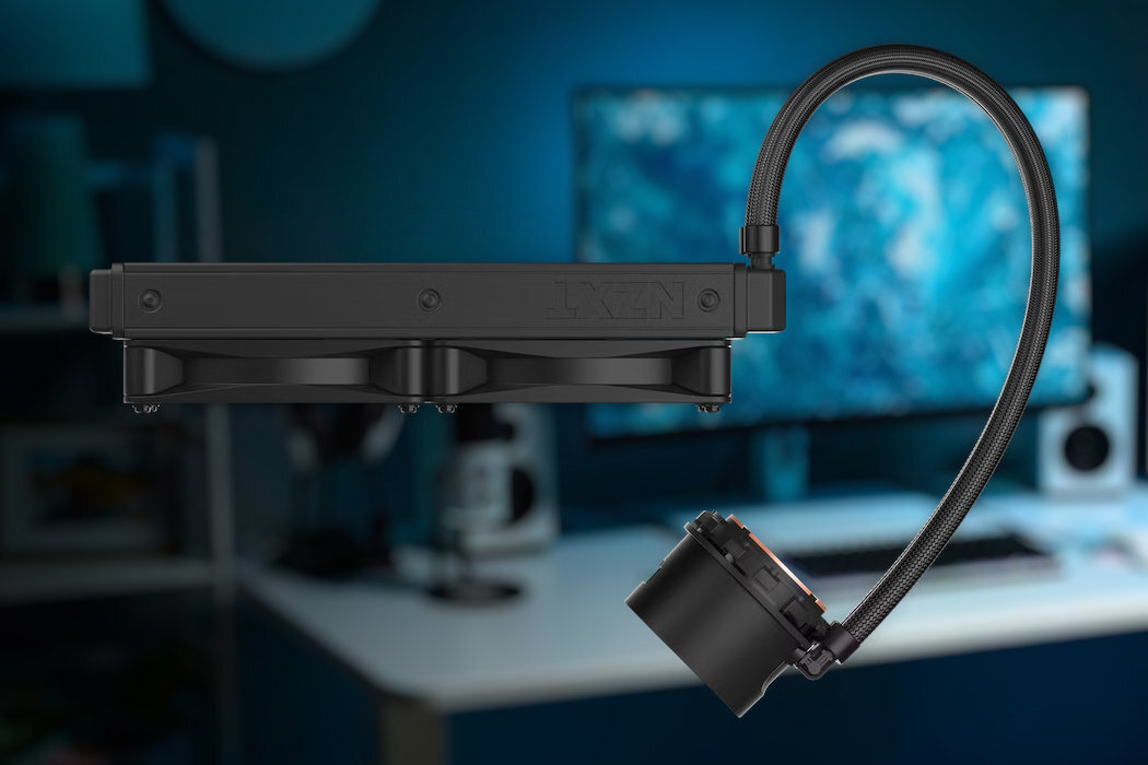 Na pierwszym planie widoczne jest chłodzenie wodne z logo NZXT, składające się z radiatora z dwoma wentylatorami i elastycznego węża. W tle rozmyty obraz biurka z monitorem i sprzętem komputerowym.