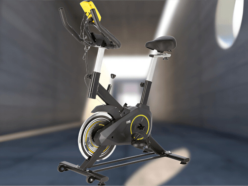 Rower spinningowy w kolorze żółtym i czarnym z widocznym logo \'ONE FITNESS\'. Znajduje się w nowoczesnym, jasnym pomieszczeniu.