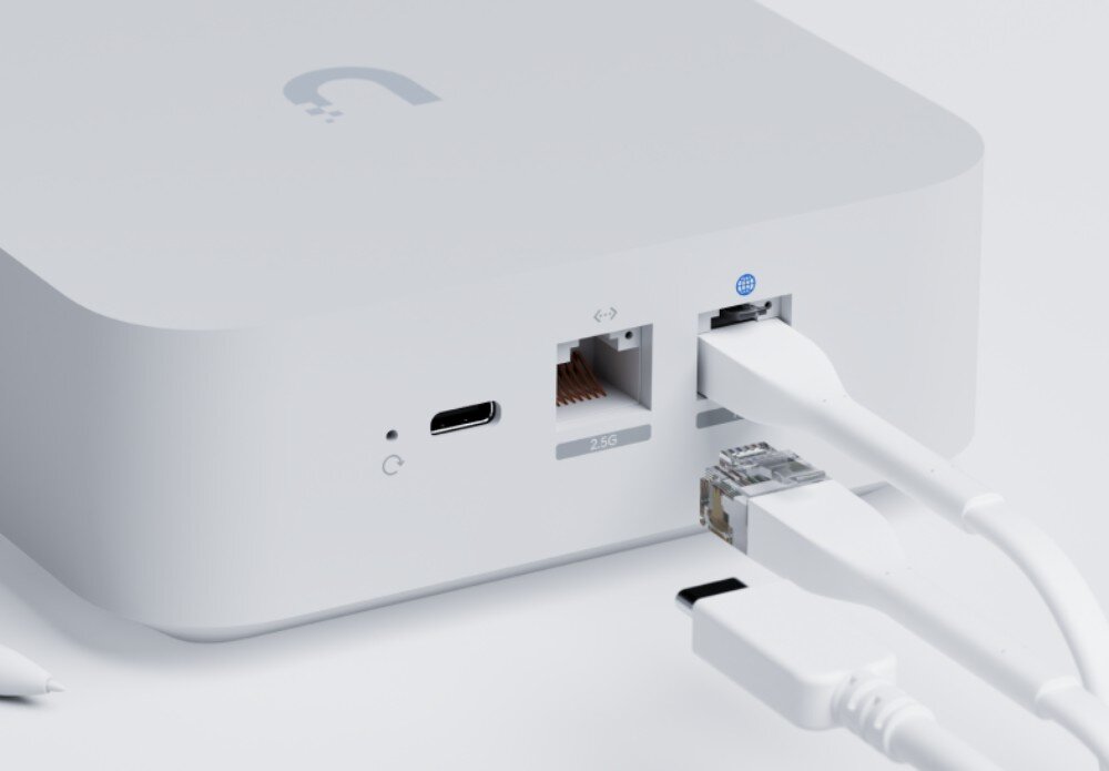 Biały router z widocznymi portami: USB-C, dwa porty Ethernet oraz podłączonymi kablami. Na górze urządzenia znajduje się logo w kształcie litery \'U\'.