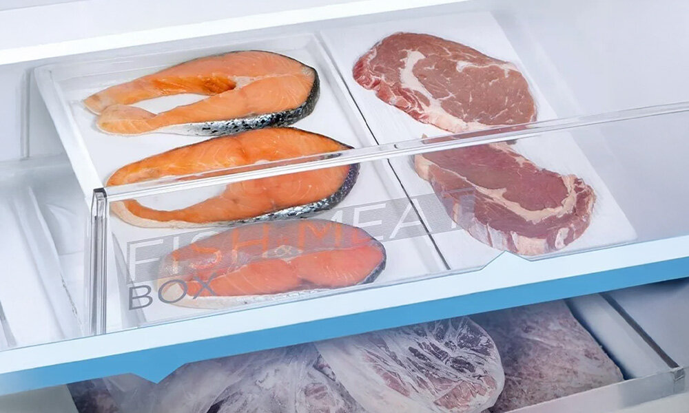 Wnętrze lodówki z szufladą oznaczoną napisem \'FISH MEAT BOX\', w której znajdują się kawałki łososia i mięsa. Poniżej widoczna jest kolejna szuflada z zamrożonymi produktami.