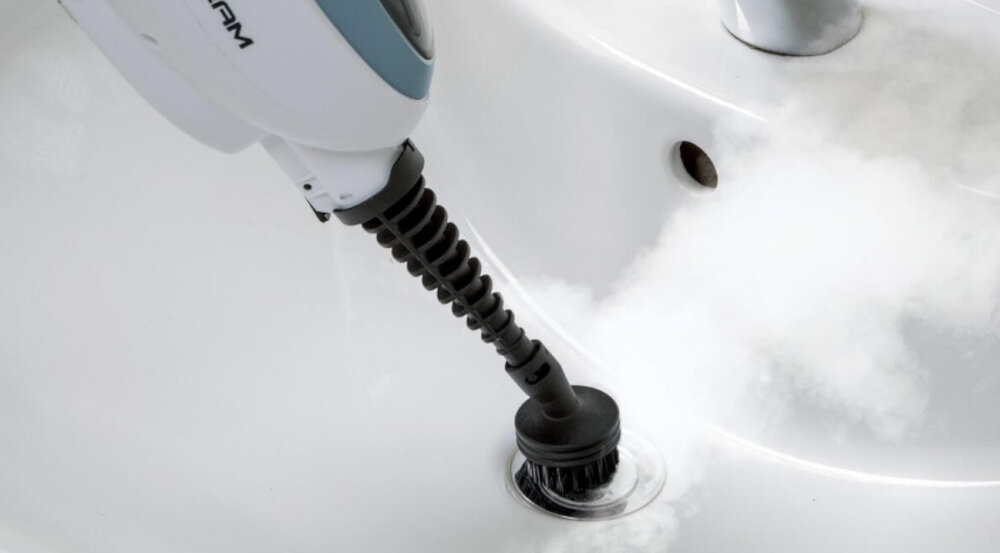 Urządzenie czyszczące z dyszą parową skierowaną na odpływ umywalki, z którego wydobywa się para. Widoczny fragment białej obudowy z napisem \'STEAM\'.