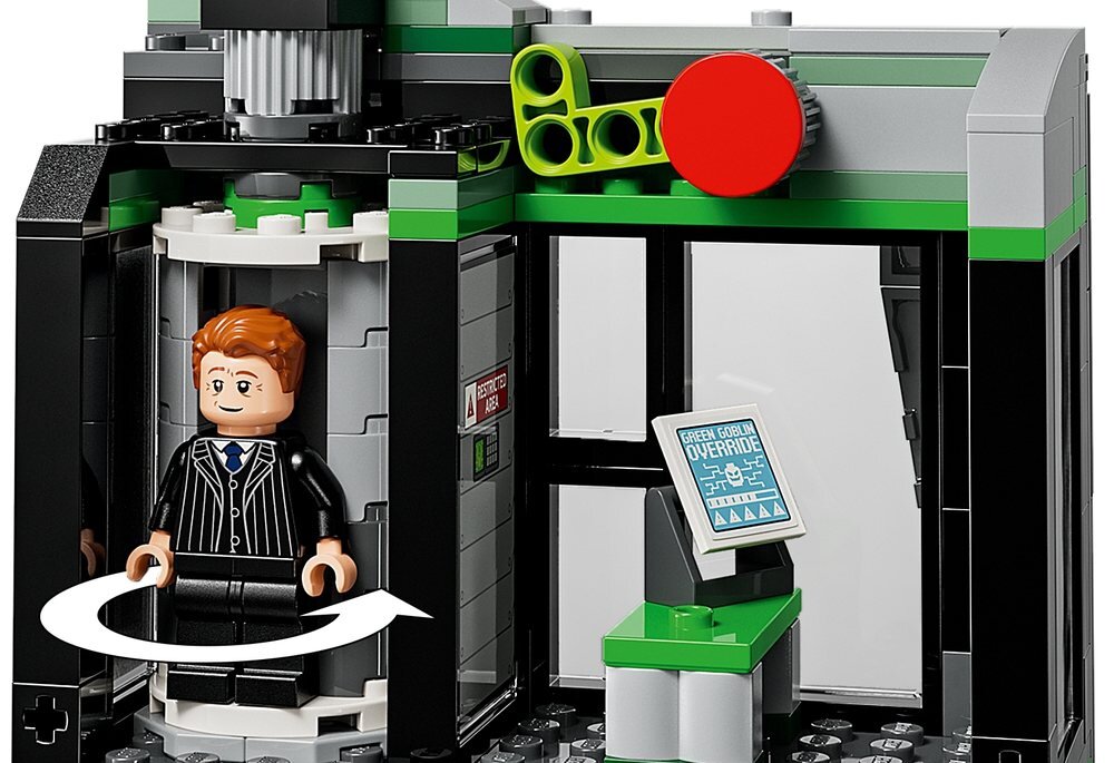 Zestaw LEGO przedstawiający wnętrze budynku z figurką w garniturze w cylindrycznej kabinie. Na ekranie widoczny jest tekst: \'GREEN GOBLIN OVERRIDE\'.