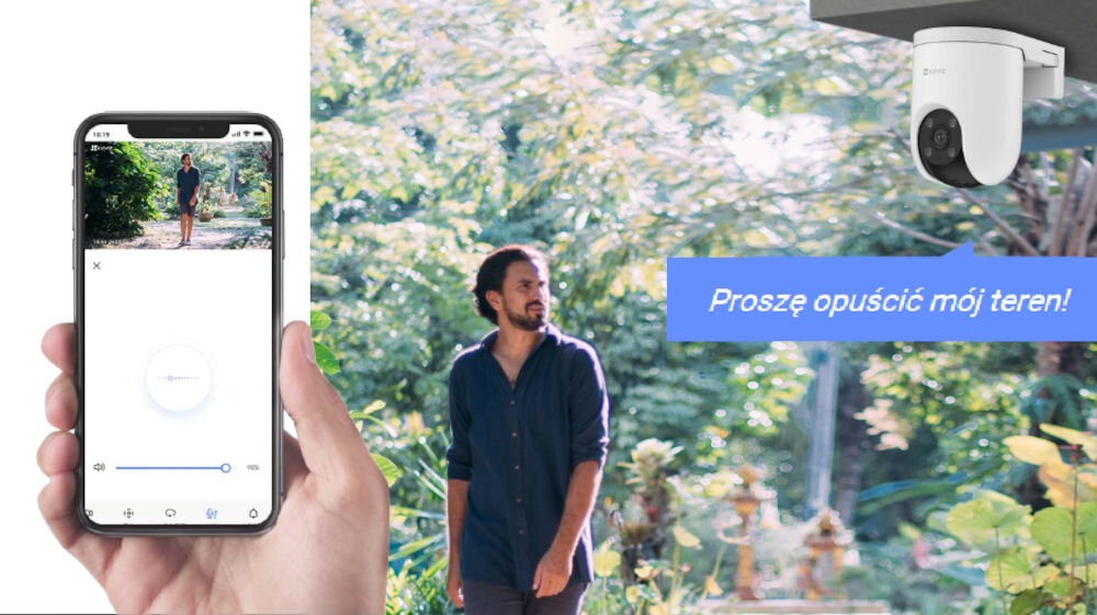 Osoba trzyma smartfon z aplikacją pokazującą obraz z kamery, obok widoczna jest zamontowana kamera zewnętrzna. Na obrazie znajduje się tekst: \'Proszę opuścić mój teren!\'.