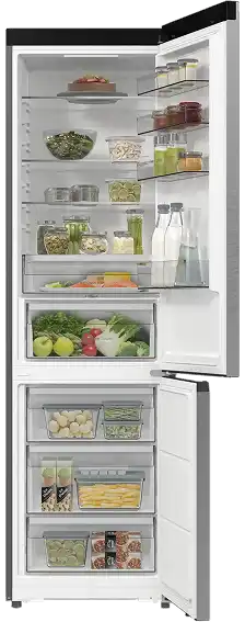 Otwarta lodówka z widocznymi półkami wypełnionymi różnorodnymi produktami spożywczymi, takimi jak warzywa, napoje i słoiki. W dolnej części znajdują się szuflady z owocami i innymi produktami.