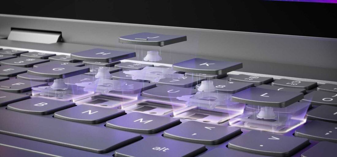 Obraz przedstawia klawiaturę laptopa z unoszącymi się klawiszami, ukazującymi mechanizm pod spodem. Widoczne są klawisze z literami J, K, U, I oraz inne, z podświetleniem w kolorze fioletowym.
