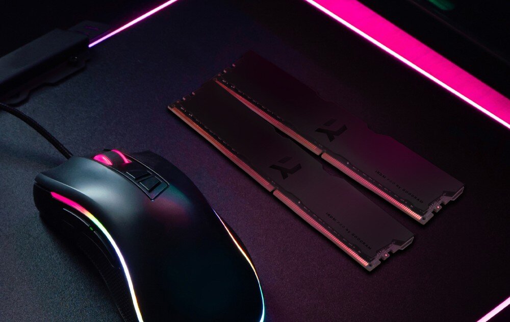 Na ciemnym biurku leży mysz komputerowa z podświetleniem RGB oraz dwa moduły pamięci RAM z czarnymi radiatorami. W tle widoczne są kolorowe paski świetlne.