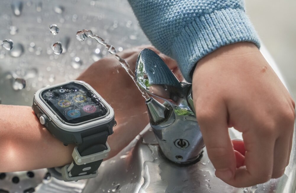 Osoba nosi smartwatch z wyświetlaczem pokazującym kolorowe ikony, a obok znajduje się kran z bieżącą wodą.
