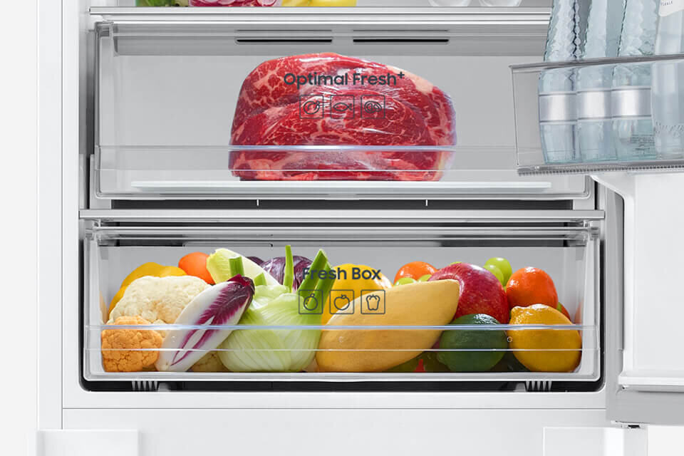 Wnętrze lodówki z dwiema przezroczystymi szufladami. Górna szuflada zawiera kawałek mięsa z napisem \'Optimal Fresh\', a dolna różnorodne warzywa i owoce z napisem \'Fresh Box\'.
