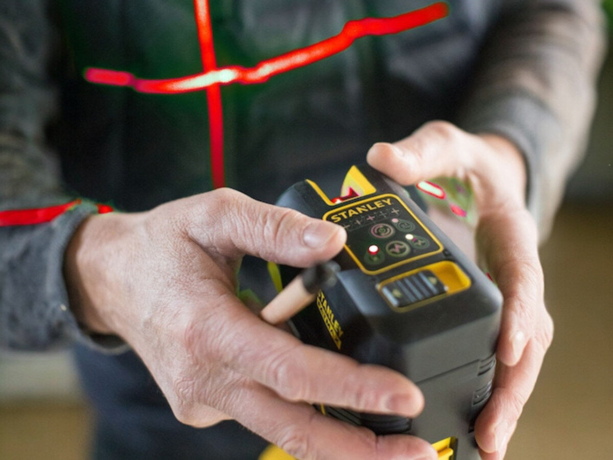 Laser punktowo-krzyżowy STANLEY FMHT1-77414, wiązka, pion, poziom, krzyż, Ręczna obsługa lasera; widoczna czerwona wiązka krzyżowa na ubraniu roboczym.