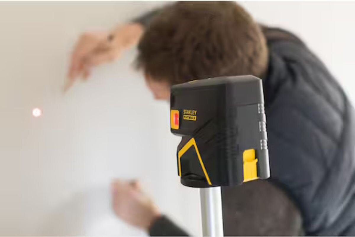 Laser punktowy STANLEY FMHT1-77413, laser, wiązka, czerwone, poziom, mężczyzna odmierza laserem punkt na ścianie