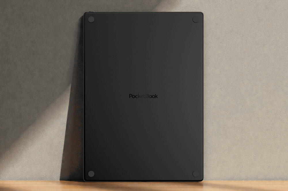 Czarny czytnik e-booków z logo \'PocketBook\' na środku tylnej obudowy, ustawiony pionowo na drewnianej powierzchni przy ścianie.