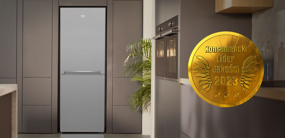 W kuchni znajduje się lodówka w kolorze inox, otoczona ciemnymi szafkami. Obok widoczny jest złoty medal z napisem \'Konsumencki Lider Jakości 2023\'.