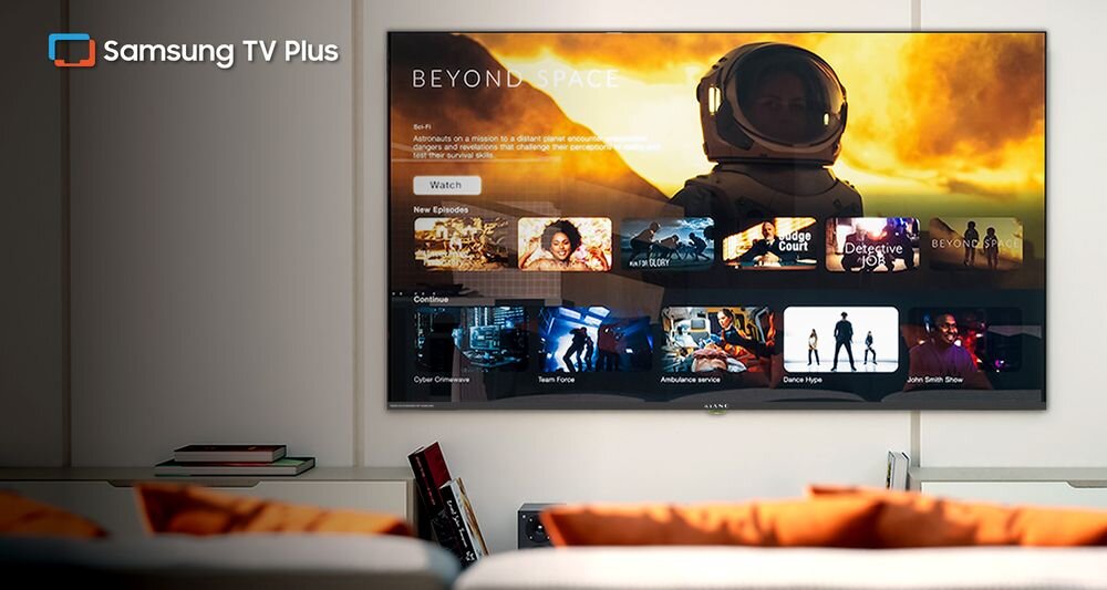 Telewizor wyświetla interfejs Samsung TV Plus z widocznymi miniaturami filmów i seriali. W lewym górnym rogu ekranu znajduje się logo Samsung TV Plus.