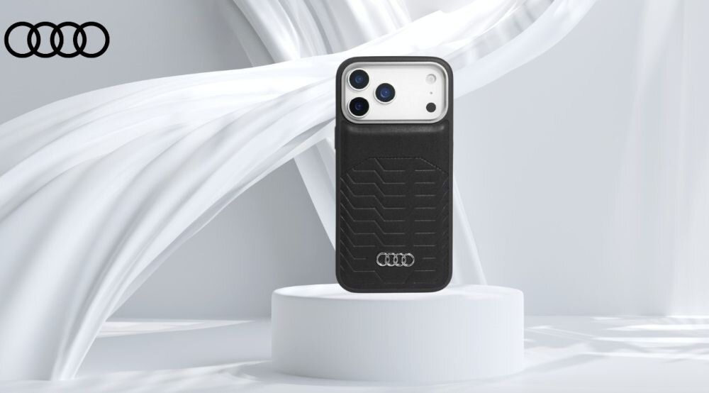Czarne etui na telefon z logo Audi umieszczone na białym postumencie. W tle widoczne są białe, falujące struktury oraz logo Audi w lewym górnym rogu.