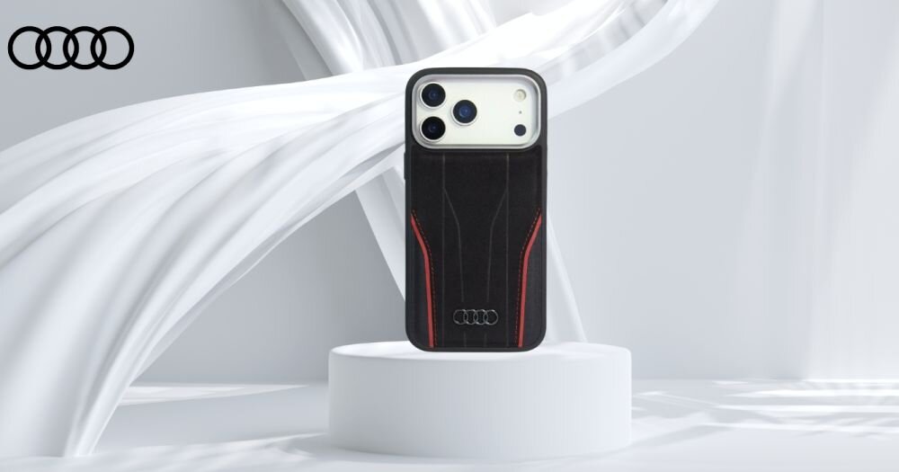 Etui na telefon w kolorze czarno-czerwonym z logo Audi, umieszczone na białym postumencie. W tle widoczne są białe, falujące elementy dekoracyjne.