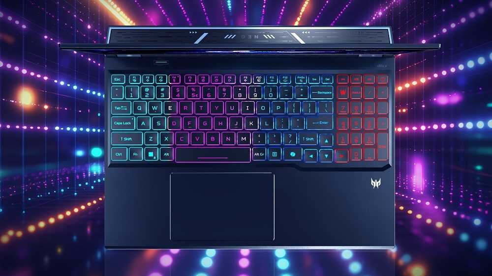 Laptop z podświetlaną klawiaturą w różnych kolorach, widoczny z góry. W tle kolorowe, rozmyte światła, a na obudowie logo producenta.