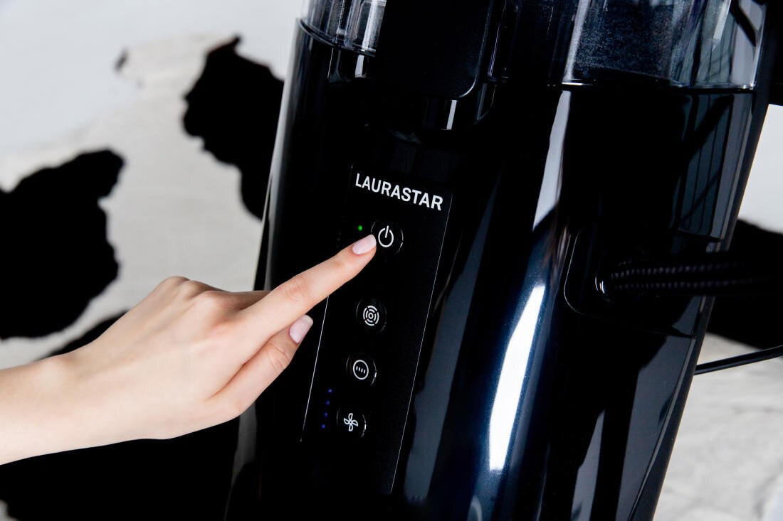 Osoba naciska przycisk zasilania na czarnym urządzeniu z widocznym logo \'LAURASTAR\'.