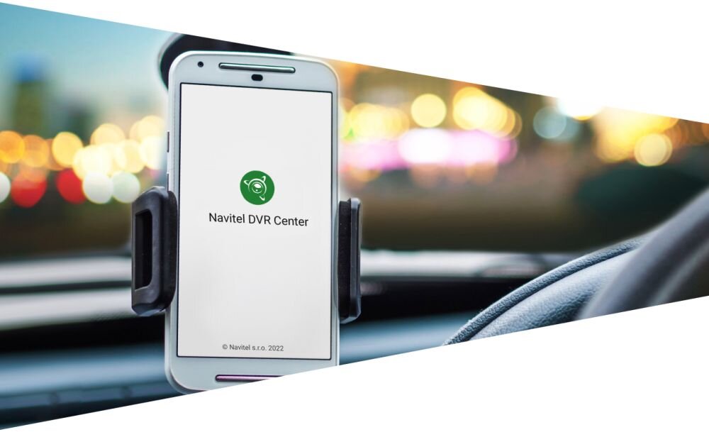 Smartfon zamocowany w uchwycie samochodowym z wyświetlonym logo Navitel DVR Center na ekranie. W tle widoczne są rozmyte światła miasta.