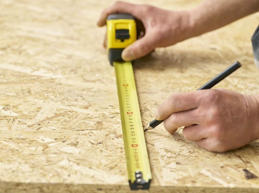 Miara zwijana STANLEY 33-720 (5 m), hak, wzmocniony, przesuwny, mobilność, osoba odmierza miarą odcinek na płycie OSB