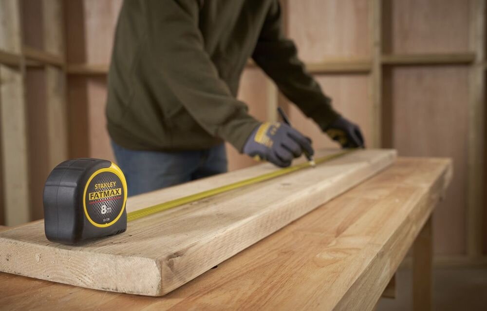 Miara zwijana STANLEY 0-33-728 (8 m), Mylar, powłoka, stabilność, czytelność, osoba odmierza miarą na stole stolarskim odcinek deski