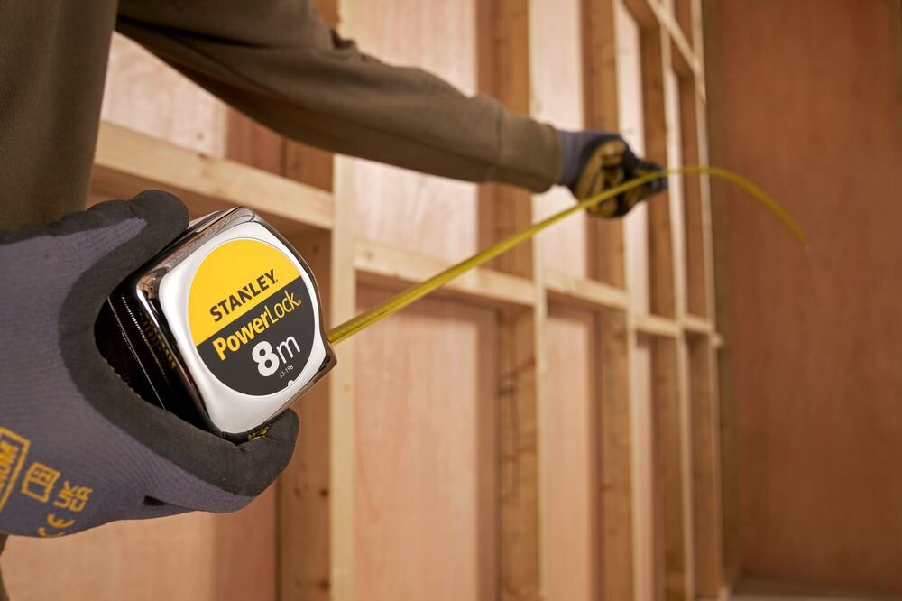Miara zwijana STANLEY 1-33-198 (8 m), precyzja, taśma, zwijanie, wytrzymałość, osoba rozwija miarę przy ścianie remontowanej
