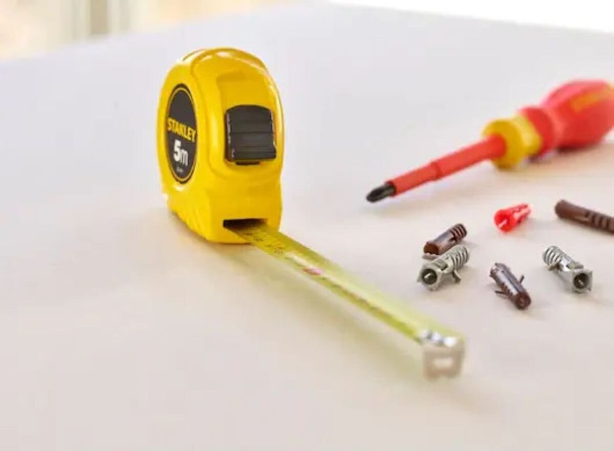 Miara zwijana STANLEY 0-30-497 (5 m), ochrona, stal, podziałka, hak, Żółta miarka zwijana STANLEY 5 m stojąca na blacie obok ołówka.