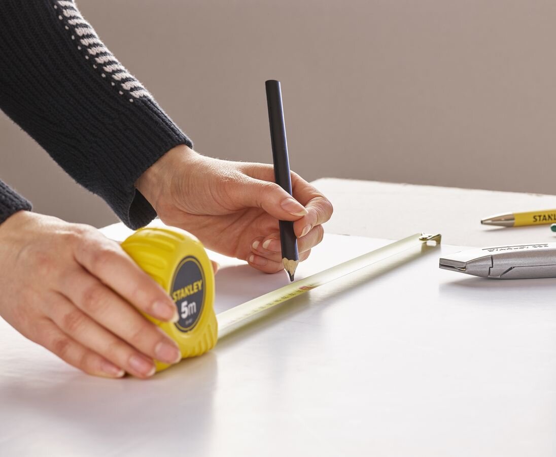 Miara zwijana STANLEY 1-30-497 (5 m), taśma, dokładność, ochrona, wygoda, osoba odmierza odcinek na blacie stołu dzięki miarce