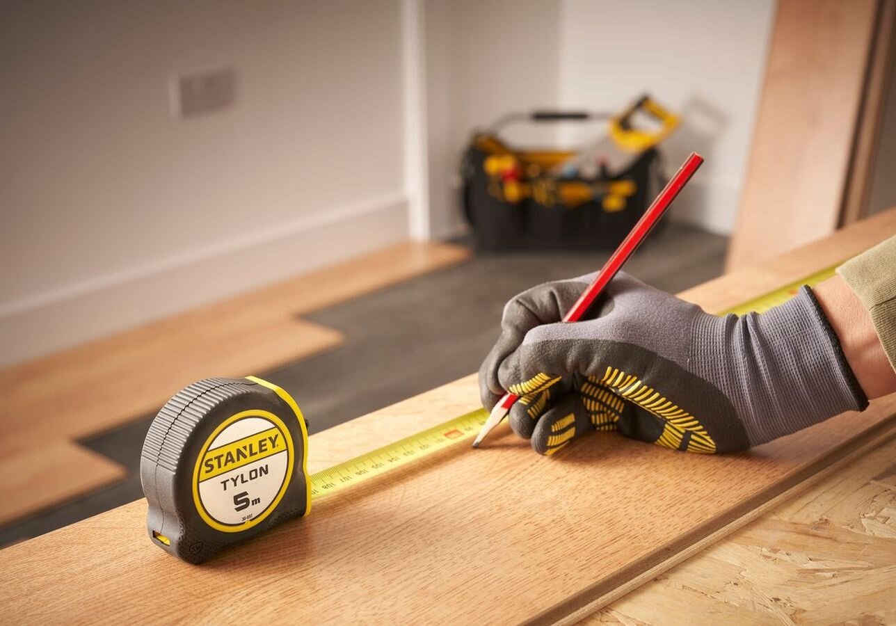 Miara zwijana STANLEY S/30-697-0, Tru-Zero, nity, krawędź, stabilność, dłoń zaznacza na wymierzonej przez miarkę desce odcinek do cięcia