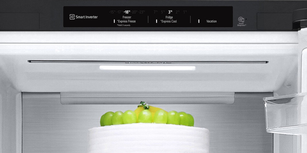 Wnętrze lodówki z widocznym ciastem na półce. Na panelu sterowania widoczny jest tekst: \'-18°C Freezer Express Freeze\', \'3°C Fridge Express Cool\', \'Vacation\'.