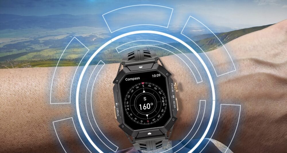 Na zdjęciu widoczny jest czarny smartwatch z wyświetlaczem pokazującym kompas z kierunkiem \'S\' i wartością \'160°\'. W tle znajduje się krajobraz górski.
