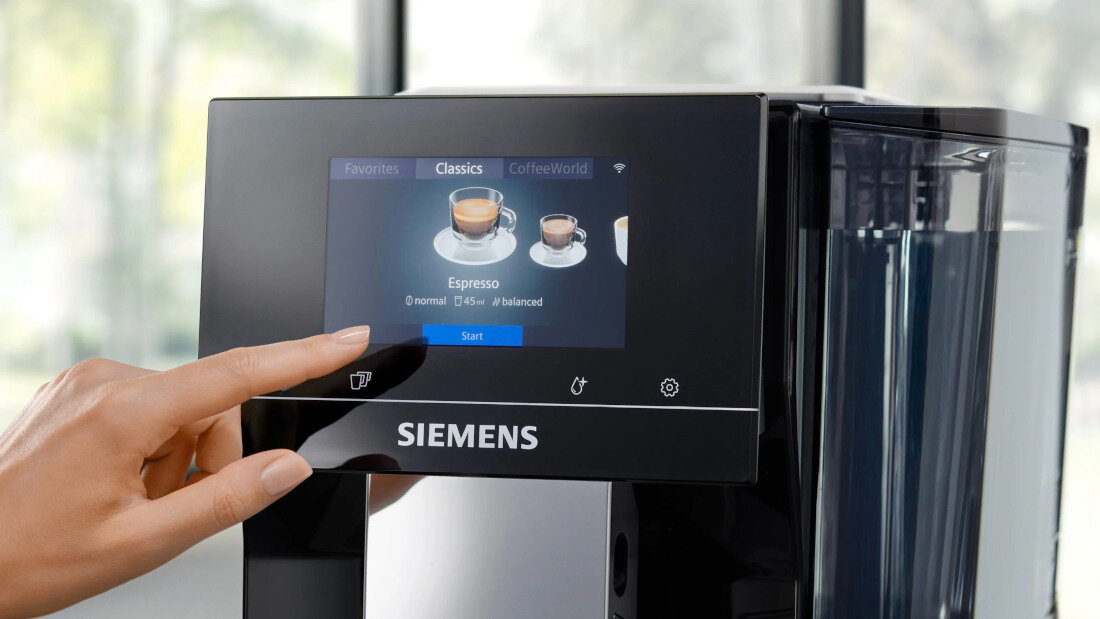 Osoba dotyka ekranu dotykowego ekspresu do kawy z widocznym logo \'SIEMENS\'. Na ekranie wyświetlane są opcje wyboru kawy, w tym \'Espresso\'.
