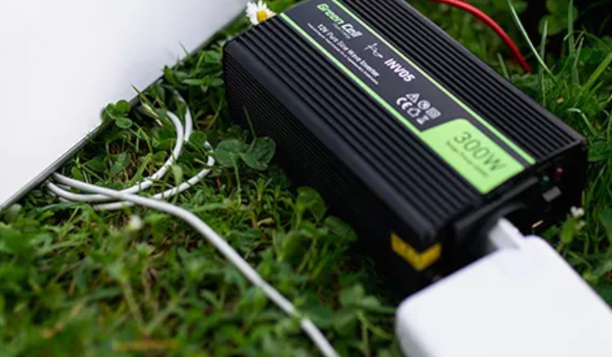 Na trawie leży czarna przetwornica z zielonym napisem \'Green Cell\' oraz oznaczeniem \'300W\'. Do urządzenia podłączony jest biały kabel.