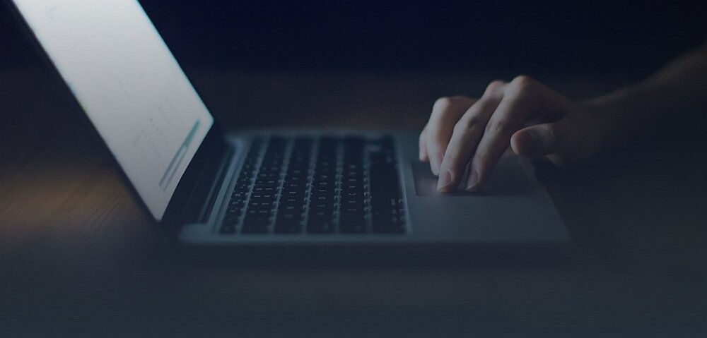 Osoba korzysta z laptopa w ciemnym otoczeniu, ekran jest lekko oświetlony.