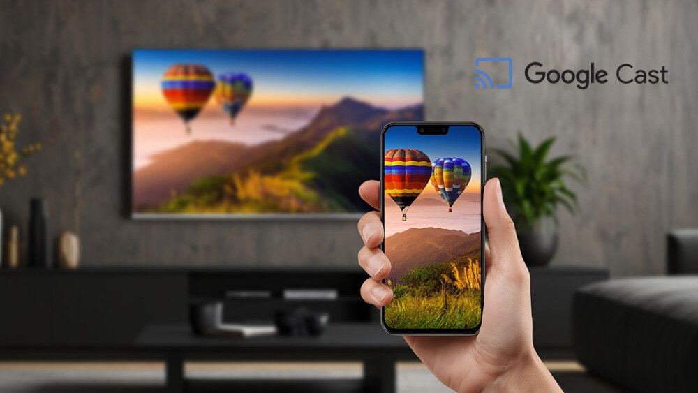 Osoba trzyma smartfon z obrazem balonów na tle gór, który jest również wyświetlany na dużym telewizorze w tle. Obok telewizora widoczne jest logo \'Google Cast\'.