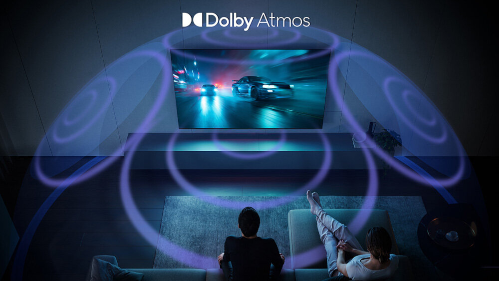 Na obrazie widać telewizor wyświetlający dynamiczną scenę z samochodami, a nad nim znajduje się napis \'Dolby Atmos\'. Przed telewizorem siedzą dwie osoby, a wokół nich widoczne są efekty dźwiękowe w postaci fal.