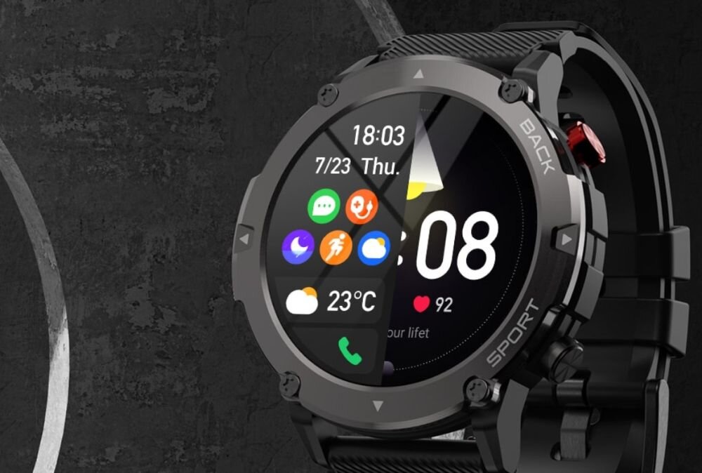 Czarny smartwatch z okrągłym wyświetlaczem pokazuje godzinę 18:03, datę 7/23, dzień tygodnia Thu., oraz ikonki aplikacji. Na ekranie widoczne są także informacje o pogodzie 23°C i liczbie kroków 92.