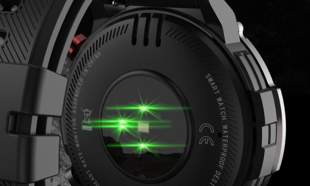 Zbliżenie na tylną część czarnego smartwatcha z widocznymi zielonymi diodami. Na obudowie znajduje się napis: \'SMART WATCH WATERPROOF DESIGN\'.