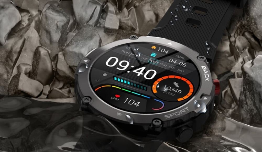 Smartwatch z okrągłym wyświetlaczem pokazuje godzinę 09:40 oraz liczbę kroków 10349. Urządzenie leży na mokrych kamieniach, a na ekranie widoczne są dodatkowe informacje, takie jak tętno 104 BPM i spalone kalorie 104 kcal.