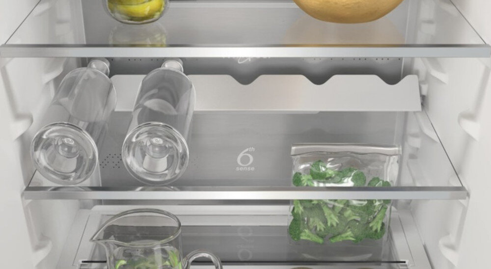 Wnętrze lodówki z trzema półkami, na których znajdują się cytryny, melon, dwie butelki, worek z sałatą i dzbanek. Na tylnej ściance widoczny jest napis \'6th sense\'.