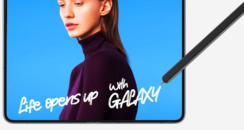 Na obrazie widoczna jest osoba w fioletowym swetrze na niebieskim tle oraz rysik dotykający ekran. Na ekranie widnieje tekst: \'Life opens up with GALAXY\'.