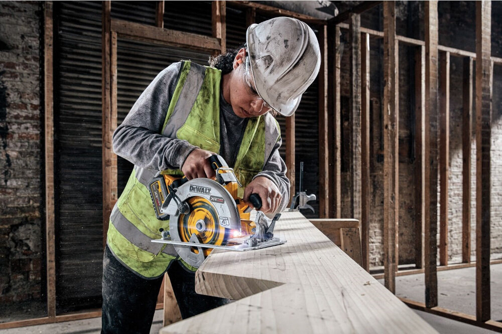 Osoba w kasku i kamizelce ochronnej używa pilarki tarczowej DEWALT do cięcia drewnianej belki. Na narzędziu widoczne jest logo DEWALT.